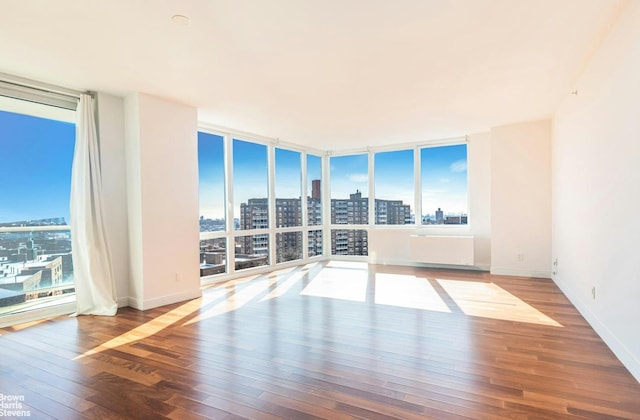 unfurnished room with a view of city, hardwood / wood-style floors, expansive windows, and baseboards