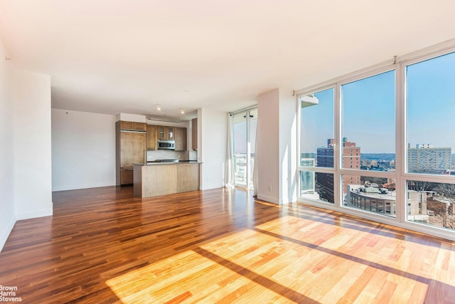 unfurnished living room with dark wood-style floors, healthy amount of natural light, a view of city, baseboards, and a wall of windows
