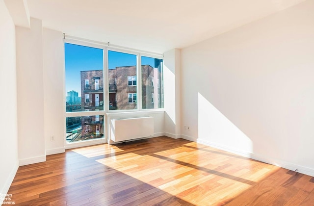 empty room featuring wood finished floors, radiator, a city view, expansive windows, and baseboards