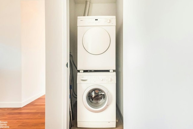 laundry room featuring stacked washer / drying machine, light wood-style floors, and baseboards