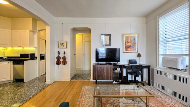 living area featuring radiator heating unit, an office area, arched walkways, light wood-type flooring, and baseboards