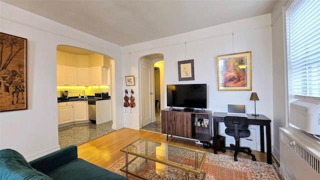 living room with radiator heating unit, arched walkways, a desk, and baseboards