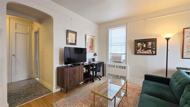 office area featuring radiator heating unit, wood finished floors, arched walkways, baseboards, and cooling unit