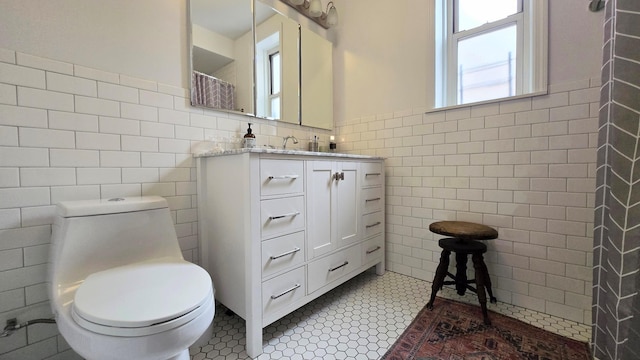 bathroom featuring tile walls, toilet, vanity, a wainscoted wall, and tile patterned floors