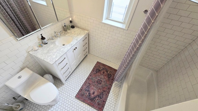 bathroom with tile walls, tiled shower, a wainscoted wall, vanity, and toilet