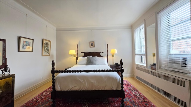 bedroom with radiator, light wood finished floors, crown molding, and baseboards