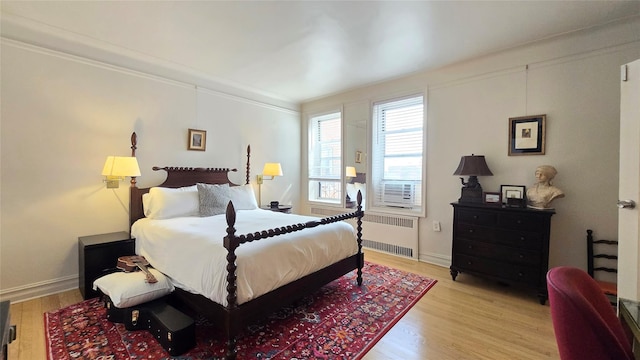 bedroom with radiator, light wood-style floors, baseboards, and ornamental molding