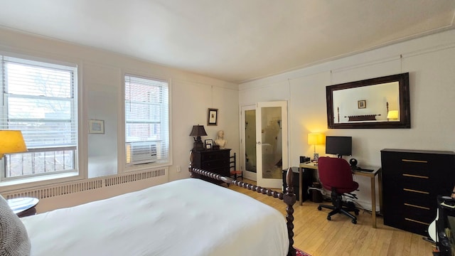 bedroom with wood finished floors, an office area, and radiator