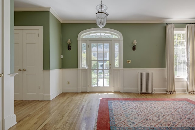 doorway to outside featuring radiator heating unit, wood finished floors, plenty of natural light, wainscoting, and crown molding