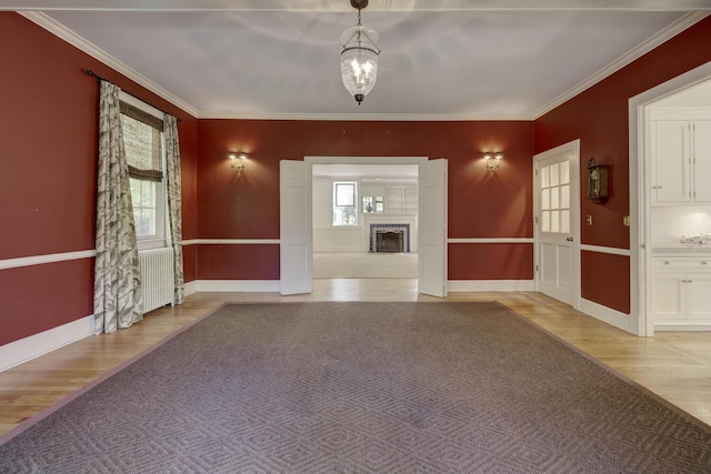 entryway with light wood finished floors, baseboards, ornamental molding, a fireplace with raised hearth, and radiator heating unit