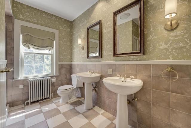 bathroom featuring radiator heating unit, toilet, wainscoting, tile walls, and a sink