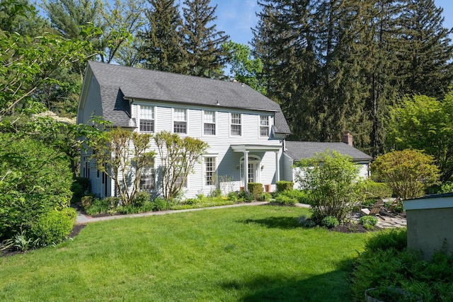 colonial house featuring a front yard and a shingled roof