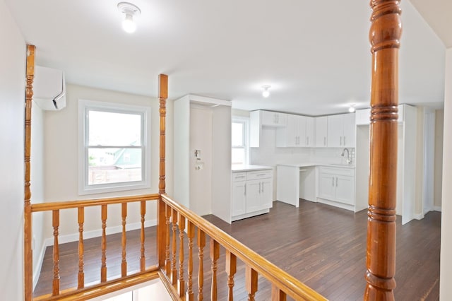 hallway featuring healthy amount of natural light, a wall mounted air conditioner, a sink, and dark wood-style floors