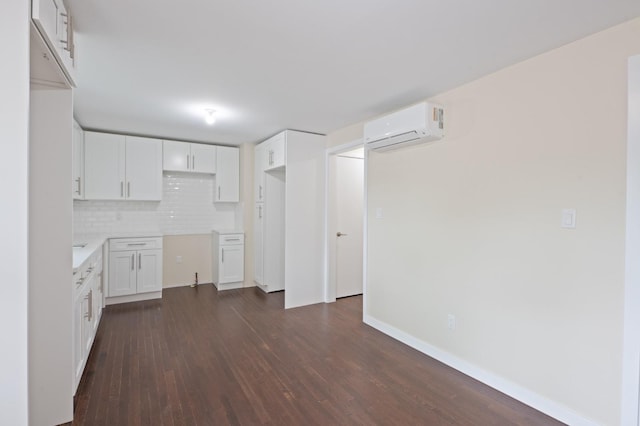kitchen featuring a wall unit AC, dark wood-style flooring, tasteful backsplash, white cabinetry, and baseboards