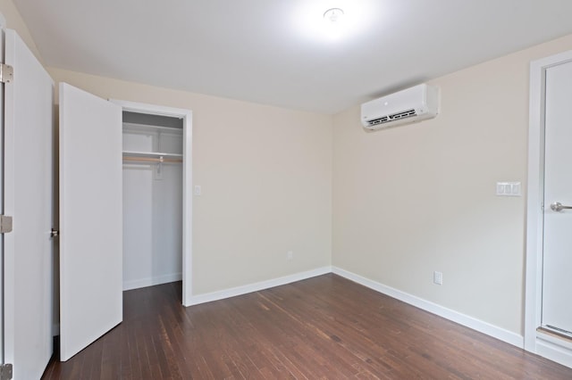 unfurnished bedroom featuring an AC wall unit, wood finished floors, baseboards, and a closet