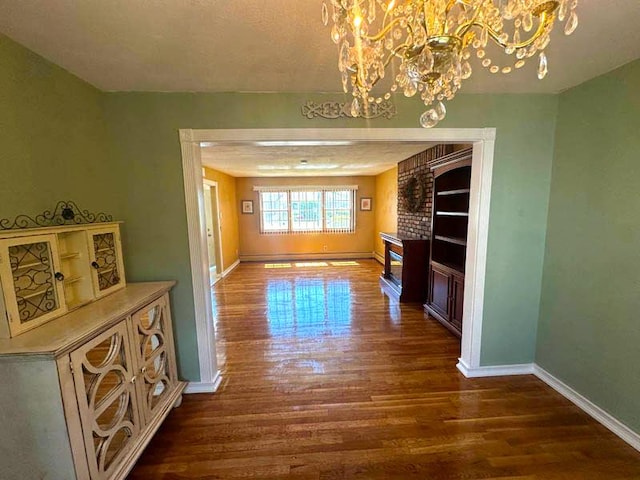 unfurnished dining area featuring wood finished floors, a chandelier, baseboards, and a brick fireplace