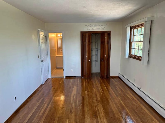 unfurnished bedroom with a baseboard heating unit, wood finished floors, and baseboards
