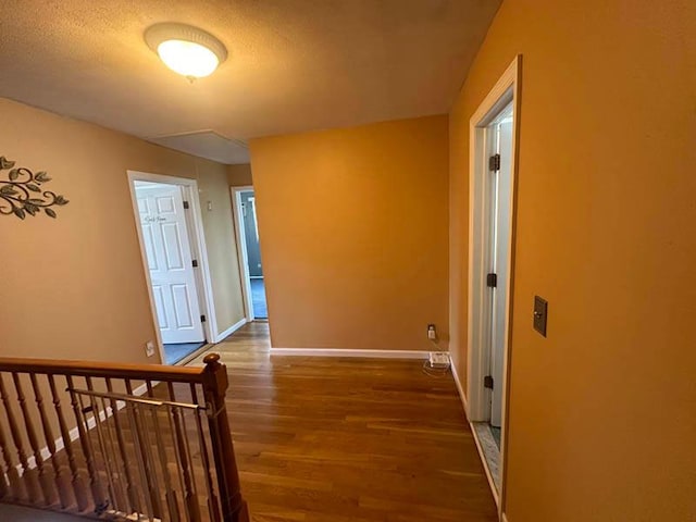 hallway featuring wood finished floors, baseboards, and an upstairs landing