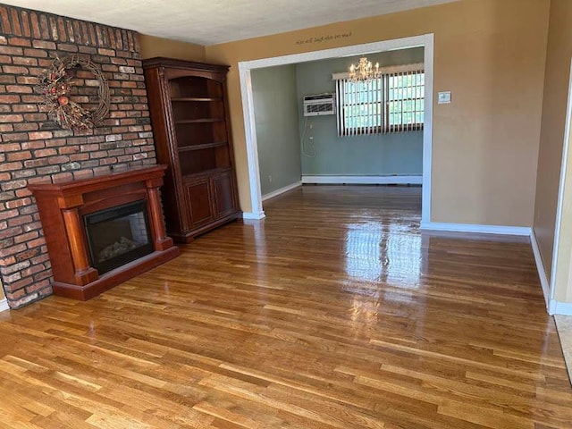 unfurnished living room featuring baseboards, a chandelier, wood finished floors, and a brick fireplace