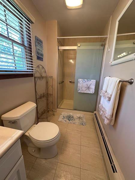bathroom with a baseboard heating unit, vanity, tile patterned flooring, and a shower stall