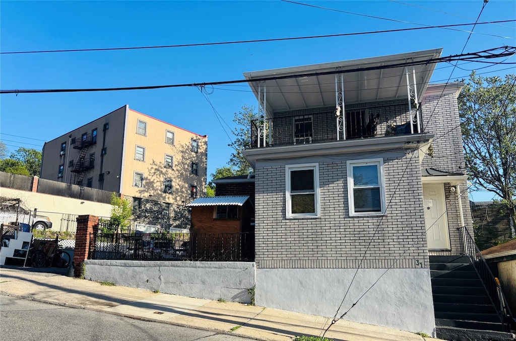 view of property exterior featuring fence, a balcony, and brick siding