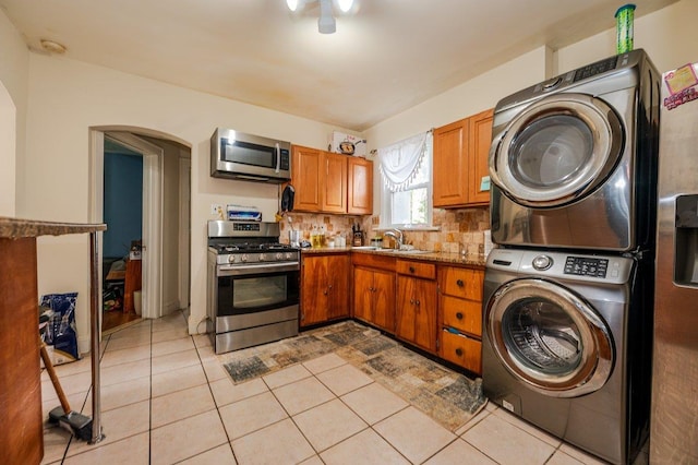 31 Thurman St, Yonkers, NY 10701 - kitchen featuring appliances with stainless steel finishes, stacked washing machine and dryer, arched walkways, brown cabinets, and tasteful backsplash