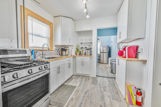 186-16 104th Ave, Saint Albans, NY 11412 - kitchen featuring appliances with stainless steel finishes, a sink, light wood-style flooring, white cabinetry, and decorative backsplash