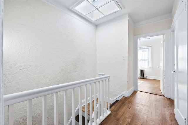 hall featuring radiator, wood finished floors, a textured wall, and baseboards