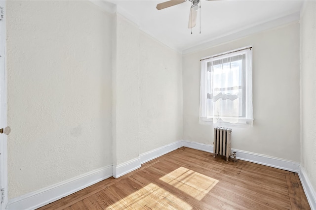 spare room with radiator, wood finished floors, baseboards, and ceiling fan