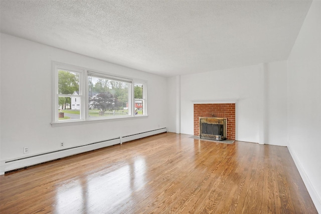 unfurnished living room with baseboard heating, wood finished floors, a fireplace, and a textured ceiling
