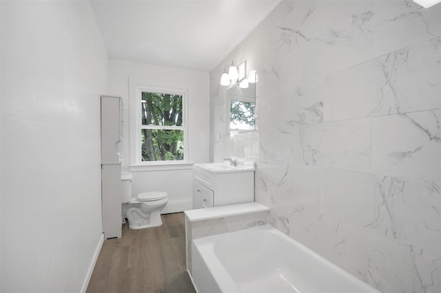 full bathroom featuring toilet, a tub to relax in, wood finished floors, vanity, and baseboards