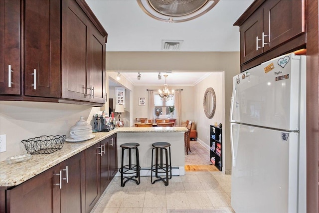 kitchen featuring freestanding refrigerator, ornamental molding, a peninsula, dark brown cabinets, and light stone counters