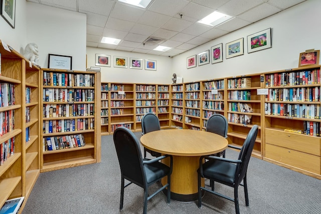 carpeted office featuring wall of books and a drop ceiling