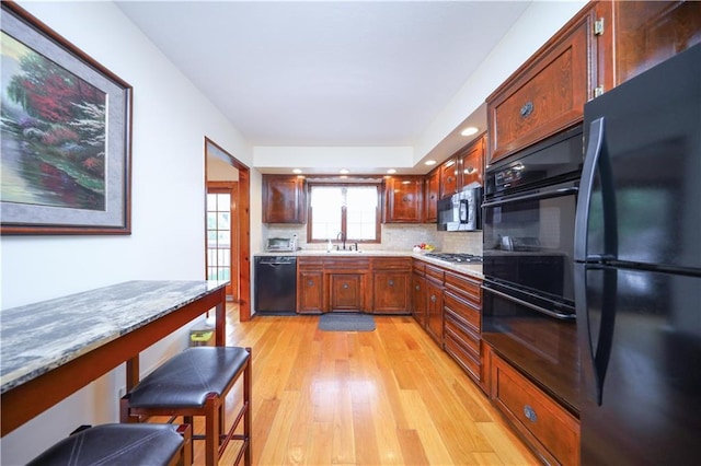 kitchen featuring black appliances, light wood-style floors, a sink, recessed lighting, and decorative backsplash