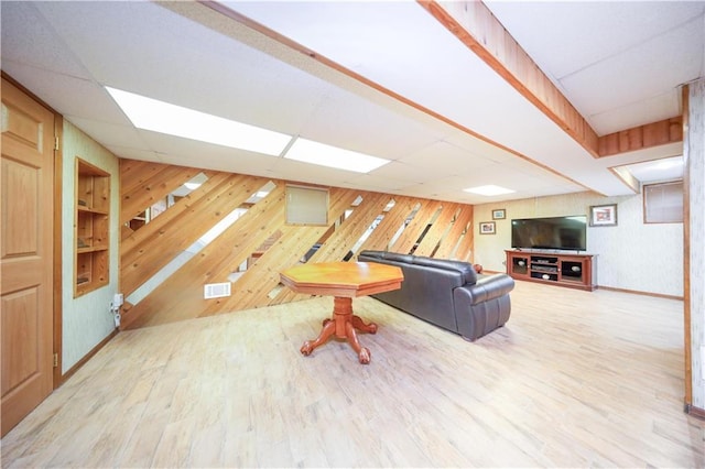 living area with a paneled ceiling, wood walls, and wood finished floors