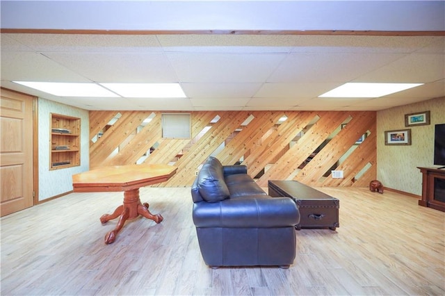 living area featuring wood walls, a drop ceiling, baseboards, wood finished floors, and built in features