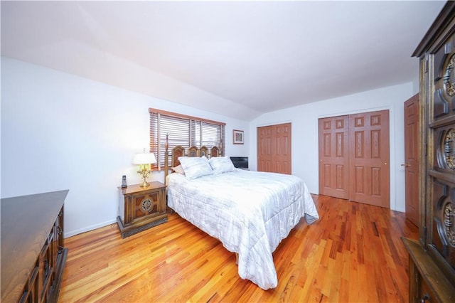 bedroom with light wood finished floors, multiple closets, baseboards, and lofted ceiling