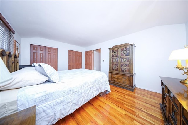 bedroom featuring light wood-style floors, vaulted ceiling, two closets, and baseboards