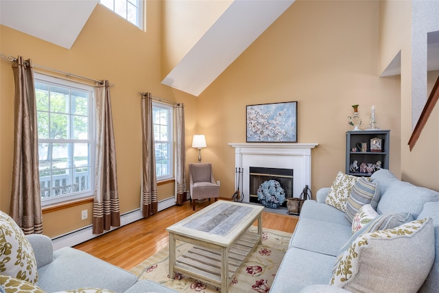 living room with high vaulted ceiling, healthy amount of natural light, a tiled fireplace, and wood finished floors