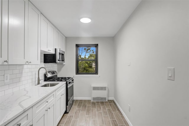 kitchen with stainless steel appliances, a sink, decorative backsplash, baseboards, and white cabinets