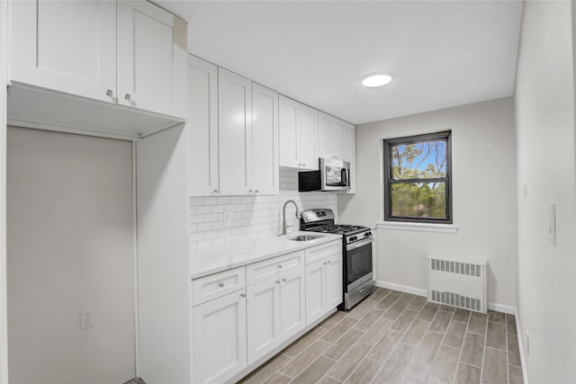 kitchen with stainless steel appliances, radiator heating unit, decorative backsplash, a sink, and baseboards