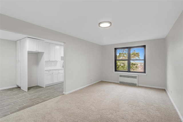 unfurnished bedroom featuring radiator, light carpet, and baseboards