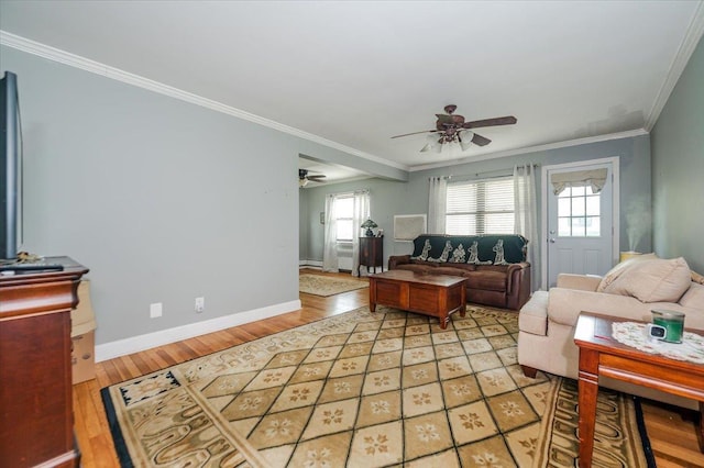 living area featuring a ceiling fan, plenty of natural light, light wood-type flooring, ornamental molding, and baseboards