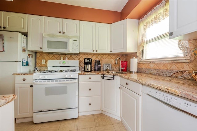 kitchen featuring white appliances, a sink, backsplash, white cabinets, and light stone countertops