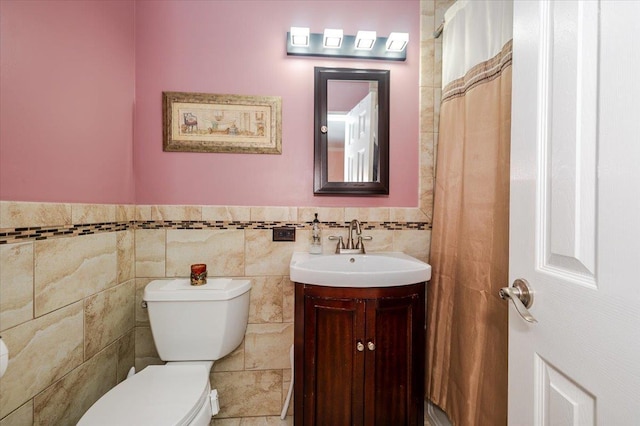 bathroom featuring tile walls, toilet, vanity, and a wainscoted wall