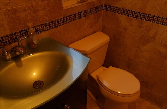 half bathroom featuring tile walls, toilet, vanity, and backsplash