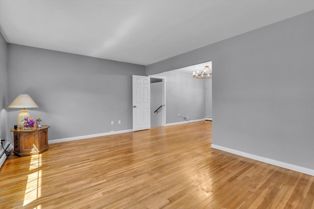 unfurnished room with light wood-style flooring, a chandelier, and baseboards