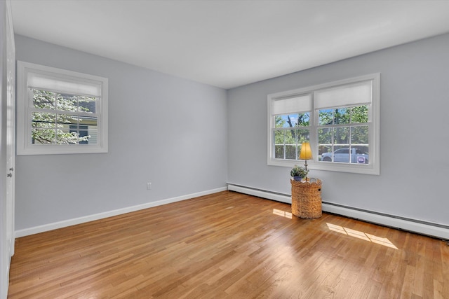 spare room featuring plenty of natural light, a baseboard radiator, light wood-type flooring, and baseboards