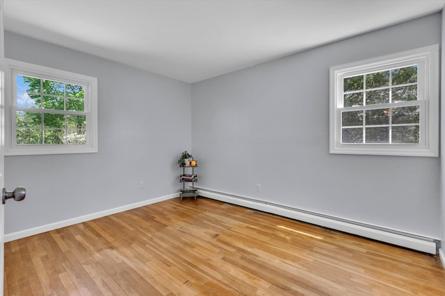 unfurnished room with a baseboard heating unit, light wood finished floors, and baseboards