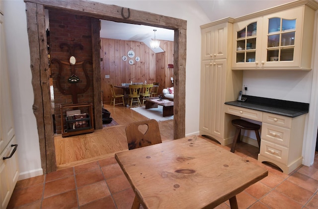 dining space featuring vaulted ceiling, baseboards, wooden walls, and light tile patterned floors